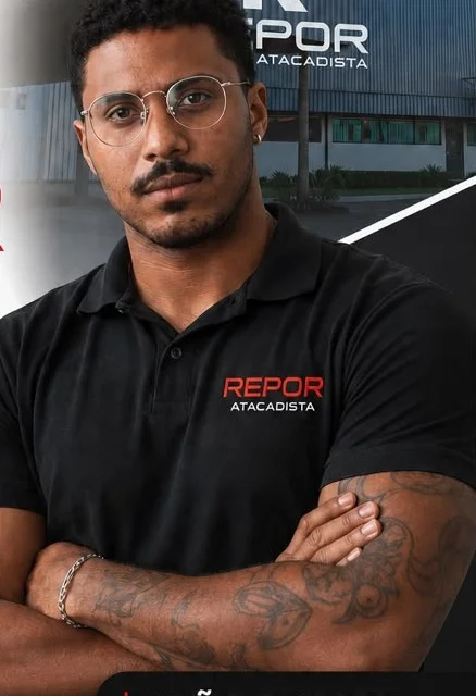 João Gabriel de braços cruzados, usando camisa polo preta da Repor Atacadista